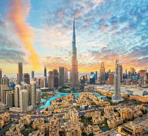 Stadtpanorama von Dubai mit dem Burj Khalifa im Zentrum, modernen Hochh&auml;usern und Wasserfl&auml;chen bei farbenfrohem Sonnenuntergang.