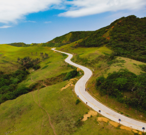 Geschwungene Stra&szlig;e f&uuml;hrt durch gr&uuml;ne H&uuml;gel und weite Landschaft mit blauem Himmel auf den abgelegenen Batanes-Inseln.