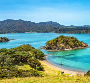 Malerische Bucht auf Neuseeland mit t&uuml;rkisblauem Wasser, kleinen Inseln und bewaldeten H&uuml;geln im Hintergrund.