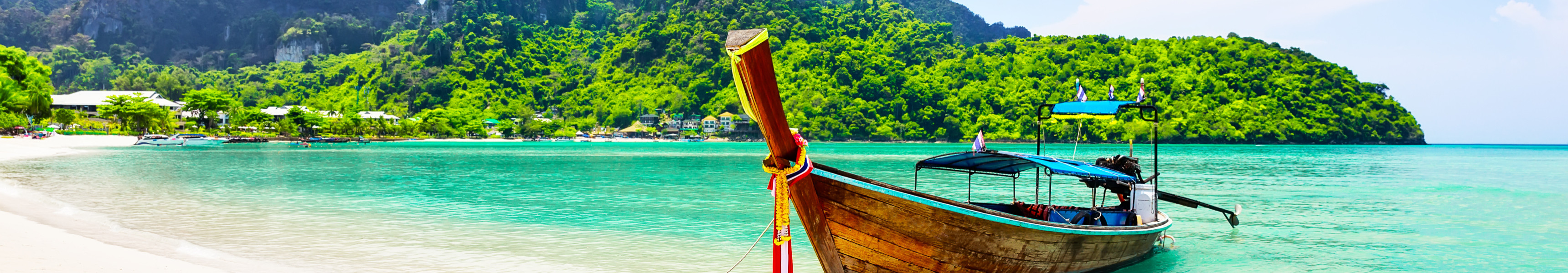 Traditionelles Longtail-Boot am weißen Sandstrand mit türkisfarbenem Wasser und grünen Bergen auf Koh Phi Phi, Thailand
