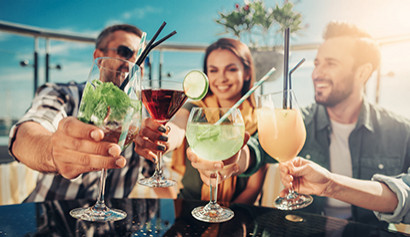 Gruppe junger Leute st&ouml;&szlig;t mit Cocktails auf einer sonnigen Rooftop-Bar an.