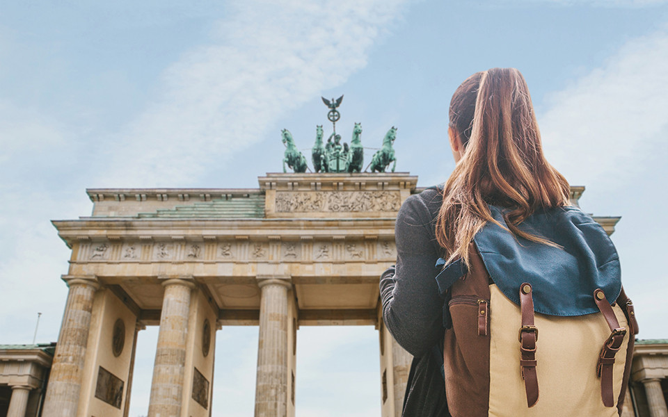 Frau mit Rucksack steht vor dem Brandenburger Tor in Berlin.